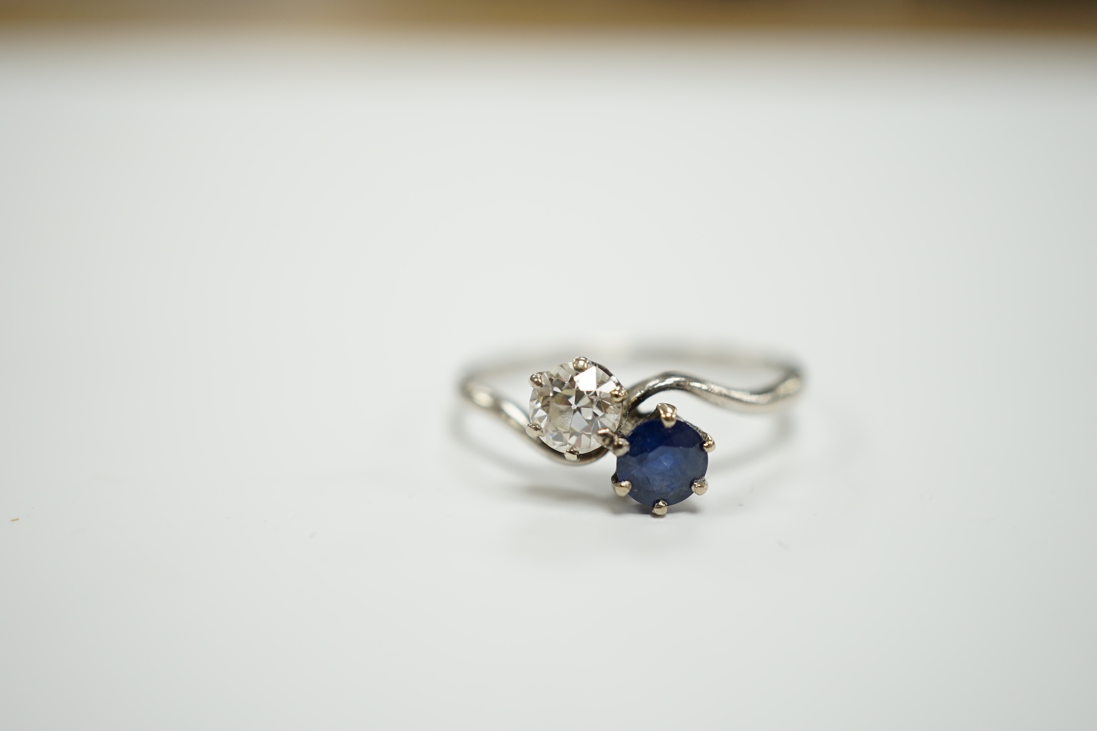 A mid 20th century white metal (stamped plat), sapphire and diamond set two stone crossover ring, size Q, gross weight 3.2 grams.